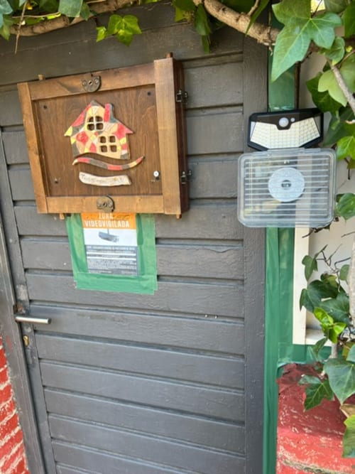 Casita para pájaros de madera con techo rojo montada en la puerta del jardín de los apartamentos Tessa en Matadepera, con luz solar y ribete verde