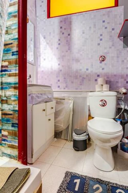Baño limpio en los apartamentos Tessa en Sabadell con inodoro blanco, lavamanos, piso de baldosas y papel pintado con patrón morado
