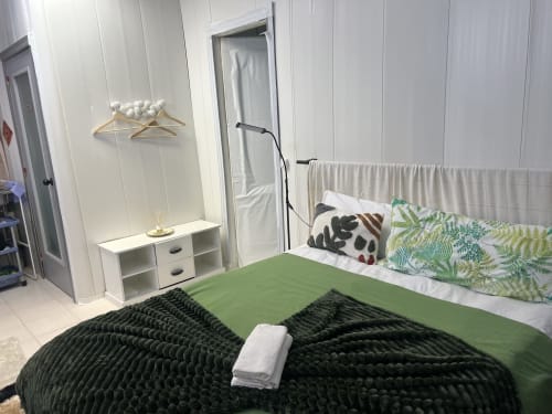 Dormitorio moderno en Apartamentos Tessa en Sabadell con ropa de cama verde, perchas de madera y mobiliario blanco minimalista