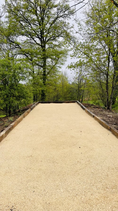 Terrain de bocce en sable entouré de verdure printanière au gîte Conciergerie Pour Tous, Corrèze