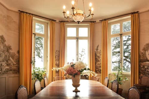 Salle à manger élégante du Château De Varambon avec rideaux dorés, lustre, fleurs fraiches et vue sur le jardin