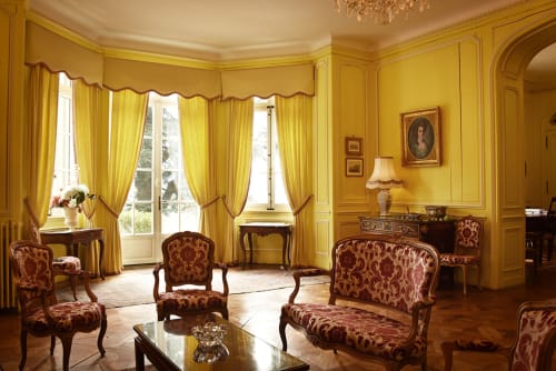 Élégant salon jaune aux chaises en velours bourgogne au Château de Varambon, avec lustre en cristal et portes-fenêtres.