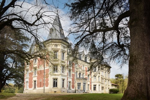 Château de Varambon, un impressionnant château en brique rouge avec tourelle, entouré d'arbres nus à Varambon, France