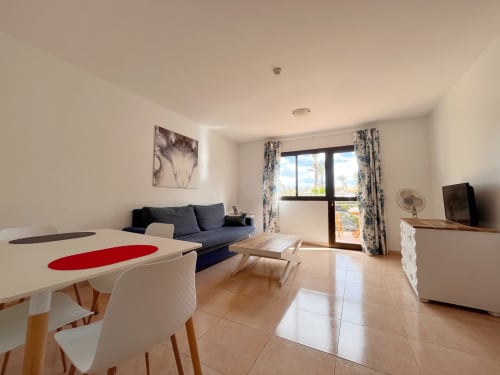 Salón moderno diáfano en apartamento vacacional La Oliva con zona de comedor, sofá y acceso a terraza