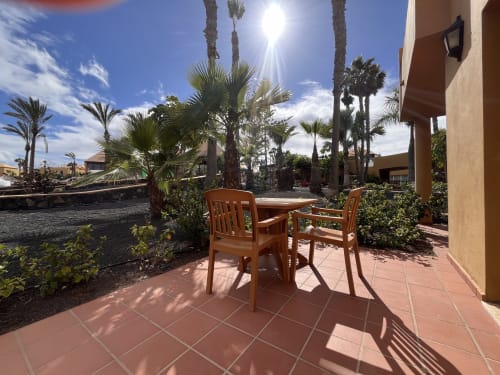 Terraza soleada con sillas y mesa de madera en FTV Holidays Homes, La Oliva, con vistas a palmeras