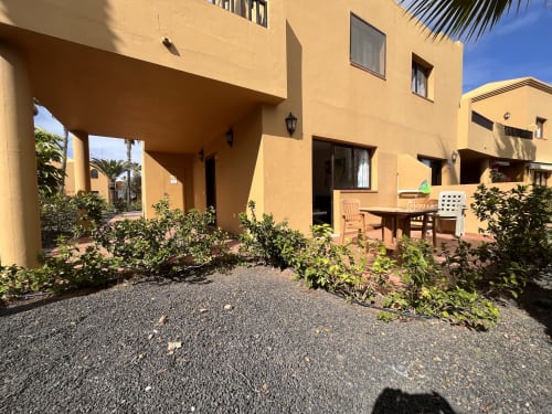 Soleada terraza de FTV Holidays Homes en La Oliva con villa amarilla, mesa de comedor y plantas mediterráneas