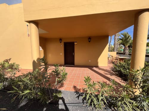 Entrada de terraza soleada de FTV Holidays Homes B&B en La Oliva con paredes amarillas, suelo de baldosas rojas y palmeras