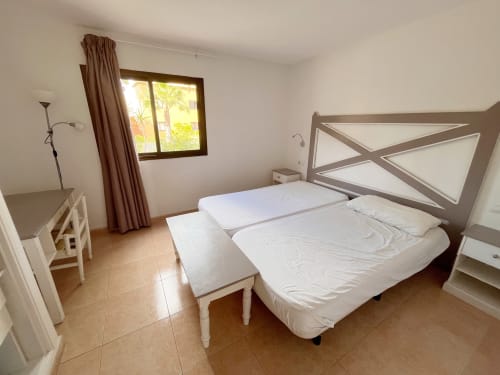 Luminosa habitación doble en FTV Holidays Homes de La Oliva con camas blancas, cortinas marrones y suelos de barro