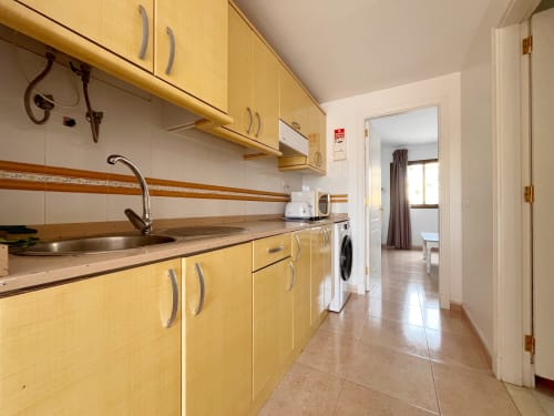 Cocina amarilla con fregadero de acero inoxidable, encimera de madera y lavadora en FTV Holidays Homes de La Oliva