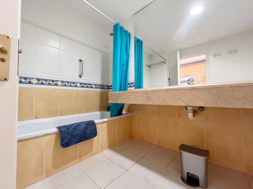 Baño espacioso con azulejos beige, cortina azul y accesorios modernos en FTV Holidays Homes, La Oliva