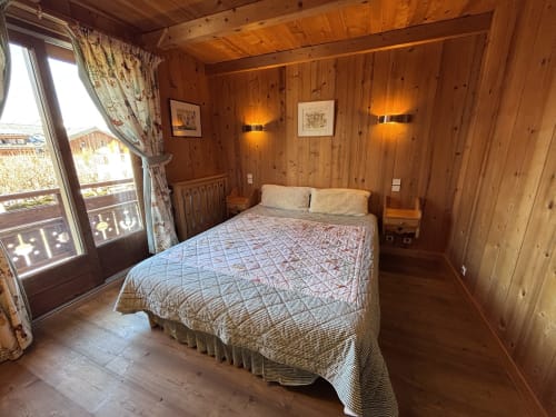 Cozy wooden bedroom with queen bed, mountain view balcony, and warm lighting at Chez Marion in Notre Dame de Bellecombe