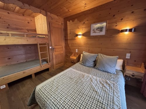 Cozy wooden cabin bedroom at Chez Marion with queen bed, bunk beds, and mountain view artwork in Notre Dame de Bellecombe