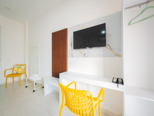 Habitación moderna de hotel con sillas amarillas, escritorio blanco, TV de pantalla plana y pared de madera en La Puerta del Angel, Ricaurte