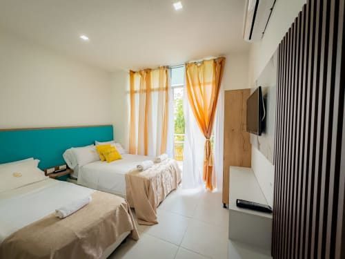 Habitación moderna del hotel La Puerta del Angel con dos camas, cabecero turquesa, cortinas naranjas y vistas al balcón en Ricaurte