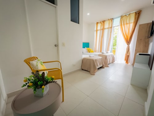 Habitación luminosa en La Puerta del Angel con camas gemelas, silla amarilla, cortinas naranjas y vistas al jardín en Ricaurte
