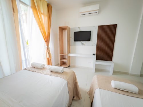 Habitación triple luminosa en el hotel La Puerta del Ángel de Ricaurte con camas doble y individual, TV, aire acondicionado y comodidades modernas.