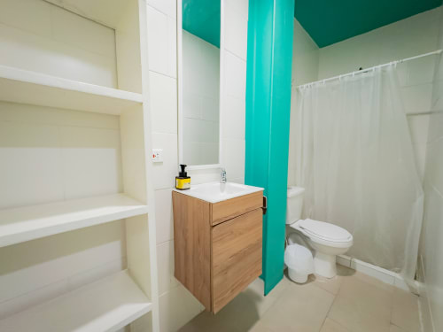 Baño moderno con tocador de madera, lavamanos blanco, pared de acento turquesa y ducha en el hotel La Puerta del Angel en Ricaurte,