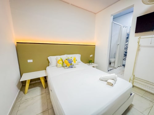 Habitación moderna en el hotel La Puerta del Ángel en Ricaurte con cama blanca, cabecero en oliva, toques amarillos y baño privado