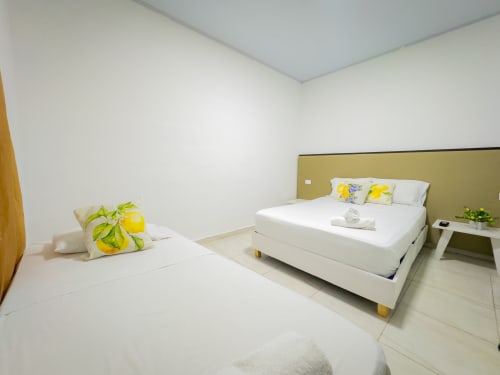 Habitación triple en el hotel La Puerta del Angel en Ricaurte con dos camas, ropa de cama blanca, almohadas amarillo limón y cabecero color oliva