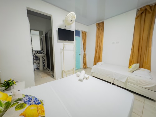 Habitación triple del hotel La Puerta del Angel en Ricaurte con camas blancas, TV, ventilador y cortinas doradas
