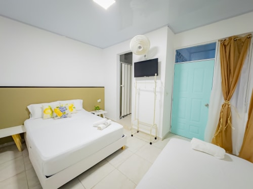 Habitación triple en Hotel La Puerta del Angel de Ricaurte con dos camas, cabecero amarillo, TV, puerta turquesa y ventilador