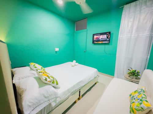 Luminosa habitación turquesa en hotel La Puerta del Angel de Ricaurte con cama doble, sábanas blancas, TV y ventilador de techo