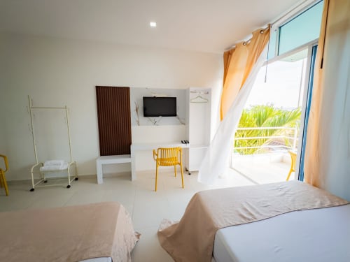 Habitación luminosa en La Puerta del Angel con dos camas dobles, TV, sillas amarillas y balcón con vistas a jardines tropicales