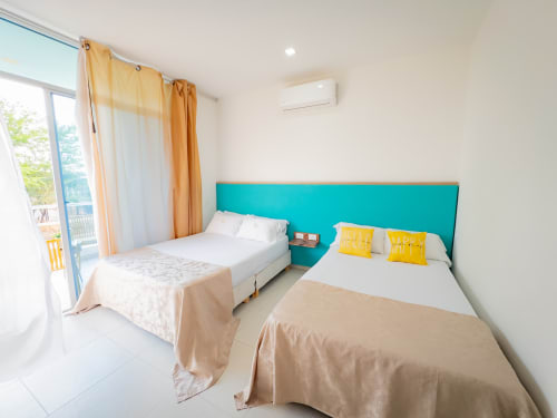 Luminosa habitación doble en el hotel La Puerta del Angel de Ricaurte con cabecero turquesa, camas gemelas, almohadas amarillas y balcón