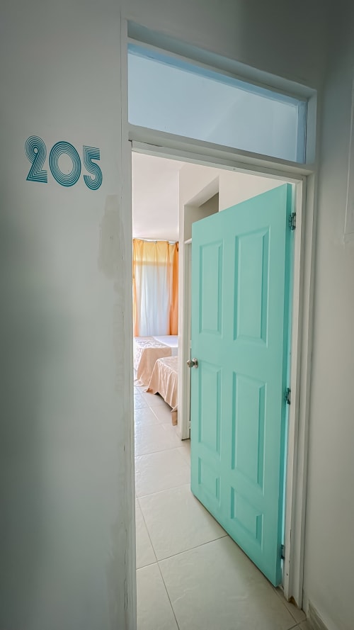 Entrada de la habitación 205 en el hotel La Puerta del Ángel en Ricaurte con puerta turquesa y vista al dormitorio