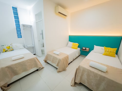 Luminosa habitación triple en La Puerta del Angel con tres camas, cabecero turquesa, almohadas amarillas, aire acondicionado y piso de cerámica