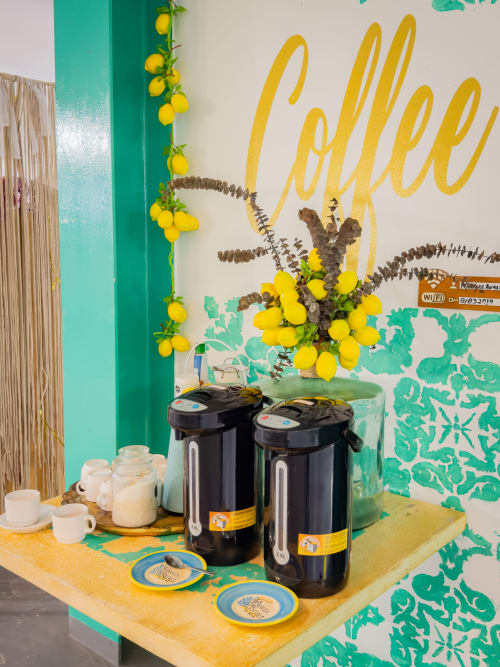 Exhibición temática de limones en el café del hotel La Puerta del Angel con guirnalda de frutas amarillas, cartel de bienvenida, termos negros y azul