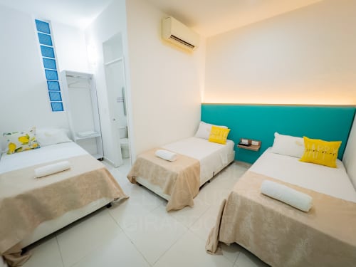 Habitación triple con aire acondicionado en el hotel La Puerta del Angel de Ricaurte, con tres camas de cabecero turquesa y amarillo