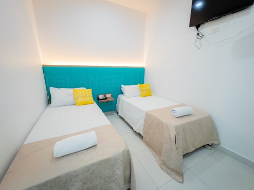 Dormitorio triple con cabecera turquesa, camas individuales, almohadas amarillas y AC en el hotel La Puerta del Angel, Ricaurte