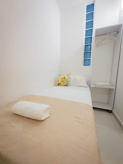 Habitación luminosa en La Puerta del Angel, Ricaurte: cama individual, sábanas blancas, almohada amarilla y unidades de ventilación azules