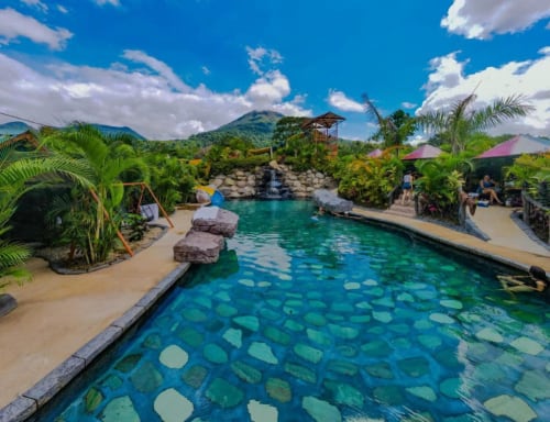 Piscina tropical del resort Cabinas Arenal Home con aguas cristalinas, palmeras y volcanes en Costa Rica