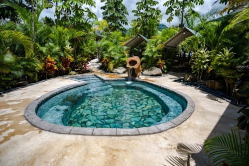 Piscina tropical en Cabinas Arenal Home, La Fortuna, Costa Rica, rodeada de exuberante vegetación y cabañas tipo tiki