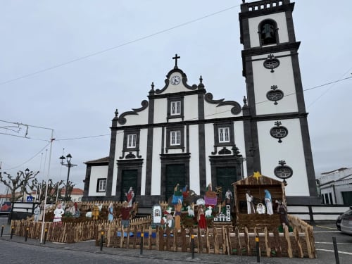Historic white and black church with tall bell tower in Ribeirinha, Portugal, featuring Christmas nativity scene display