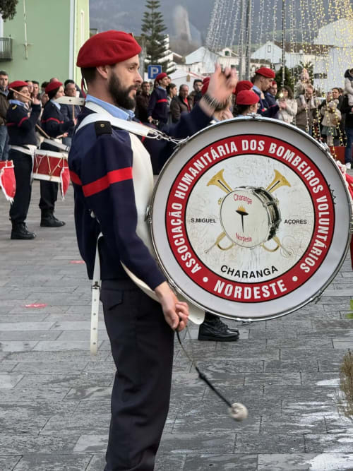 Marching band drummer in red beret playing bass drum at Charanga parade in Ribeirinha, Azores