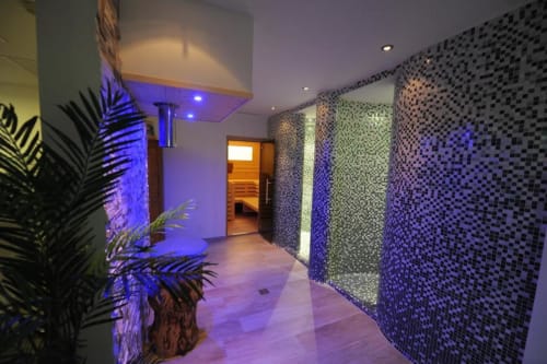 Moderner Spa-Flur im Rustclea Apartments in Selva di Valgardena mit Mosaikwänden, blauer Beleuchtung und Topfpflanzen.