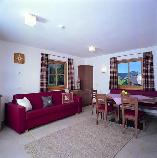 Bright living area at Rustclea Apartments in Selva di Valgardena with burgundy sofa, wooden furniture, and mountain views