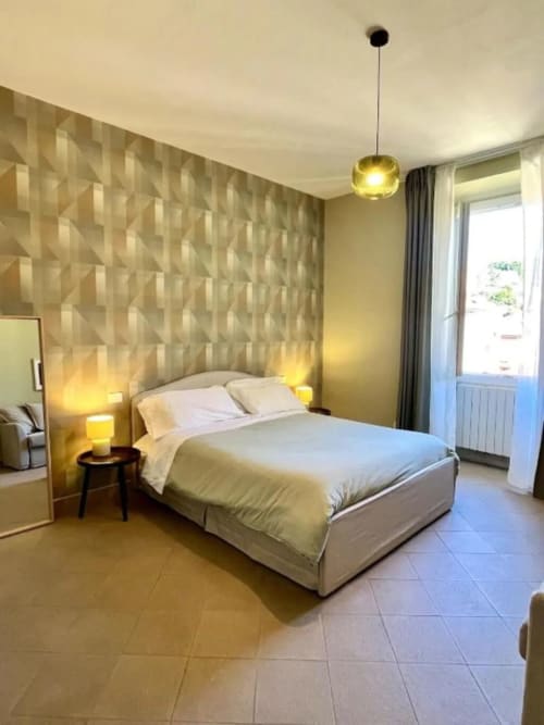 Camera da letto moderna con parete geometrica, illuminazione a sospensione e porta in vetro verso il balcone dell'appartamento Downtown Srl Roma