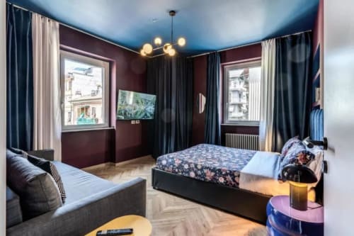 Camera da letto di moderno appartamento romano con pareti bordeaux, soffitto blu, letti gemelli, divano e vista sulla città