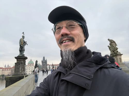 Man smiling on Charles Bridge in Prague with historic architecture and statues in background