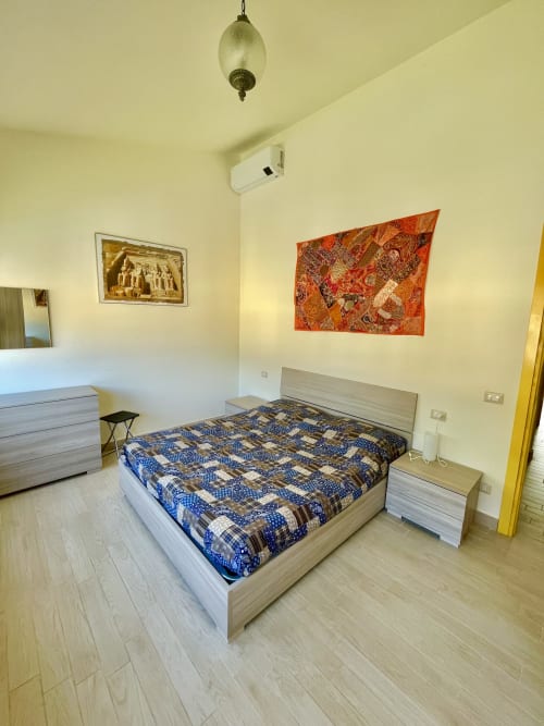 Modern bedroom with light wood bed, blue patterned comforter, and orange wall tapestry at Varenna by Foot apartment in Italy