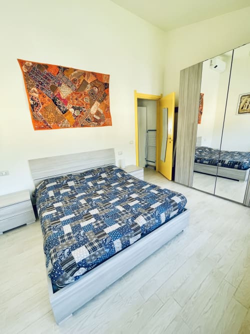 Modern bedroom at Varenna by Foot with white bed, blue patterned comforter, yellow door, and mirrored wardrobe in Varenna,