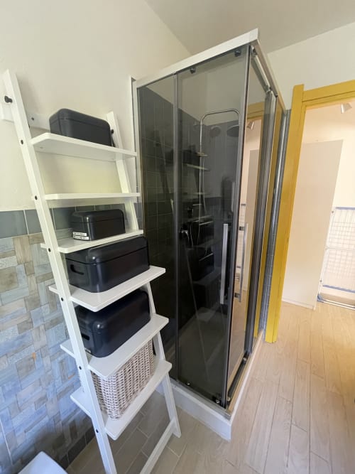 Modern bathroom in Xerxe's House apartment, Varenna, with glass shower enclosure and white shelving unit with black storage