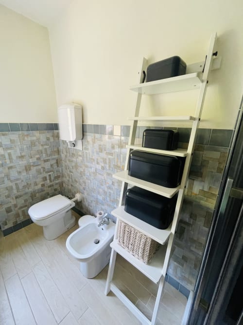 Modern bathroom in Varenna apartment with toilet, bidet, tile backsplash, white shelving unit with black storage bins, and
