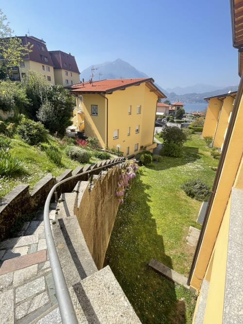 Bright yellow apartment building in Varenna with mountain lake views, terraced gardens, and stone pathways