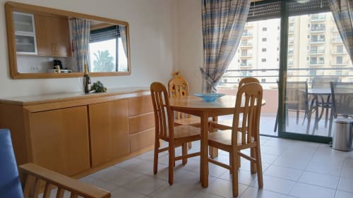 Sala de jantar moderna no apartamento Sweet Home Portimão com mesa de madeira, cadeiras, kitchenette e acesso à varanda com vista para a cidade