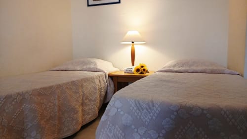 Duas camas de solteiro com roupas de cama bege no apartamento Sweet Home, Portimão. Criado-mudo de madeira com luminária e girassóis.